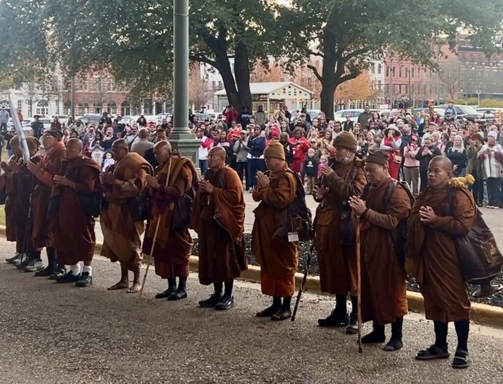 PHOTOS: Walk for Peace monks make extended stop in Montgomery 2 Monks wearing orange and red pray while hundreds of people stand silently behind them